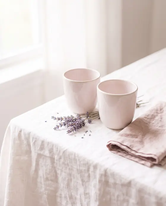 Zwei helle Keramiktassen nebeneinander auf einer Leinendecke mit Lavendel